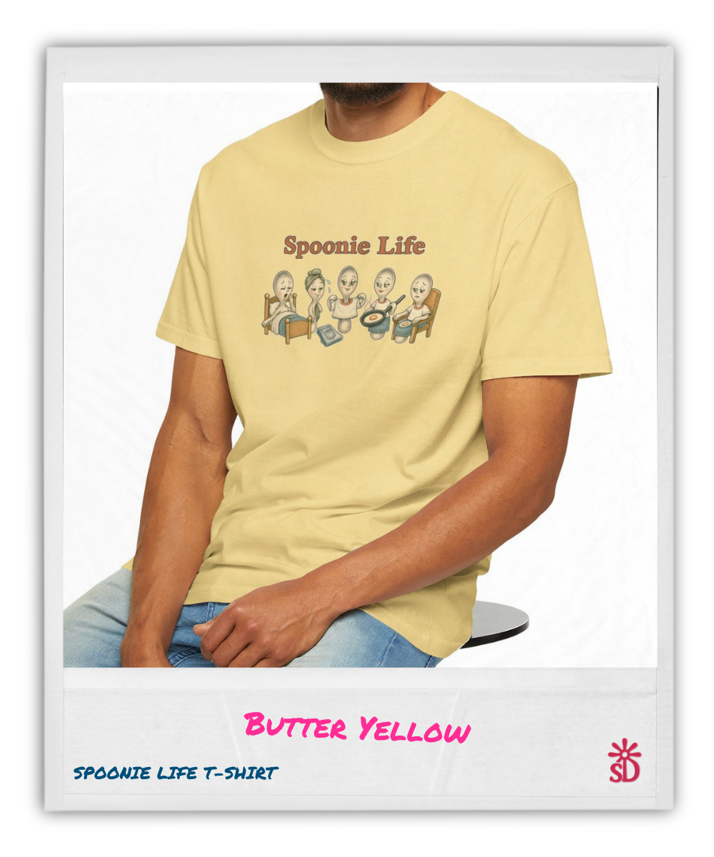 Person wearing a yellow 'Spoonie Life' t-shirt with cartoon characters, sitting on a chair.